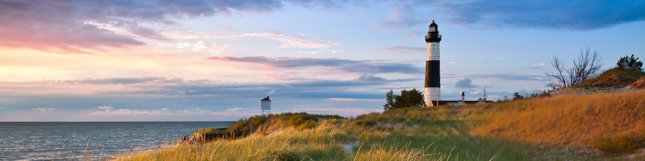 A Michigan lighthouse at the end of a pier reaching out over the water at sunset.
